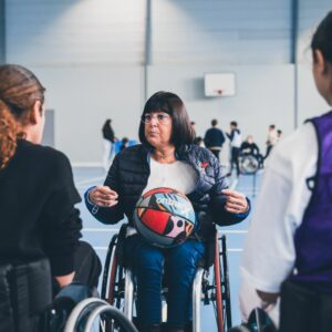 Personne expliquant à des élèves en face d'elle le rugby fauteuil.