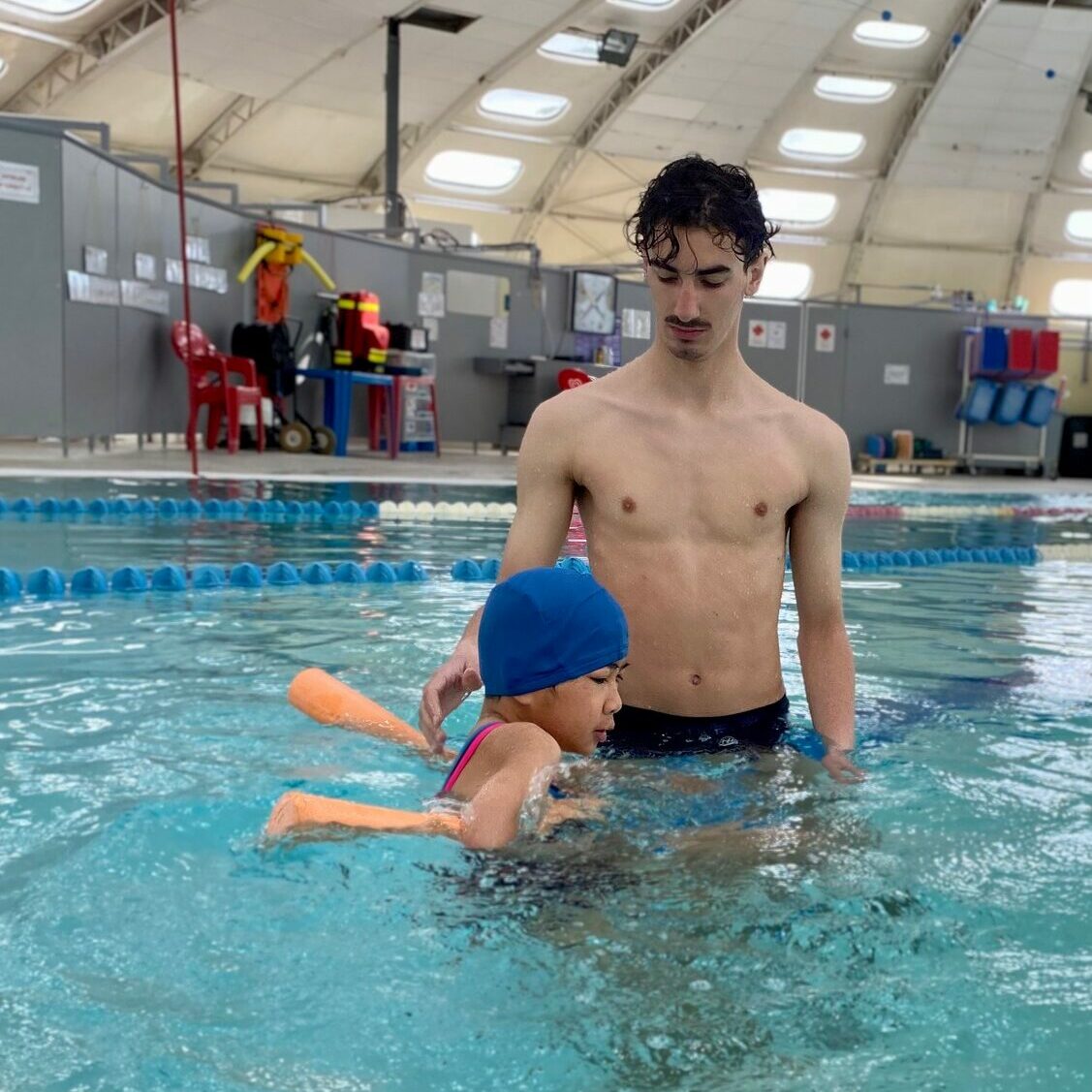 Adulte à la piscine apprenant à un enfant à se déplacer dans l'eau à l'aide d'une frite, pris de côté