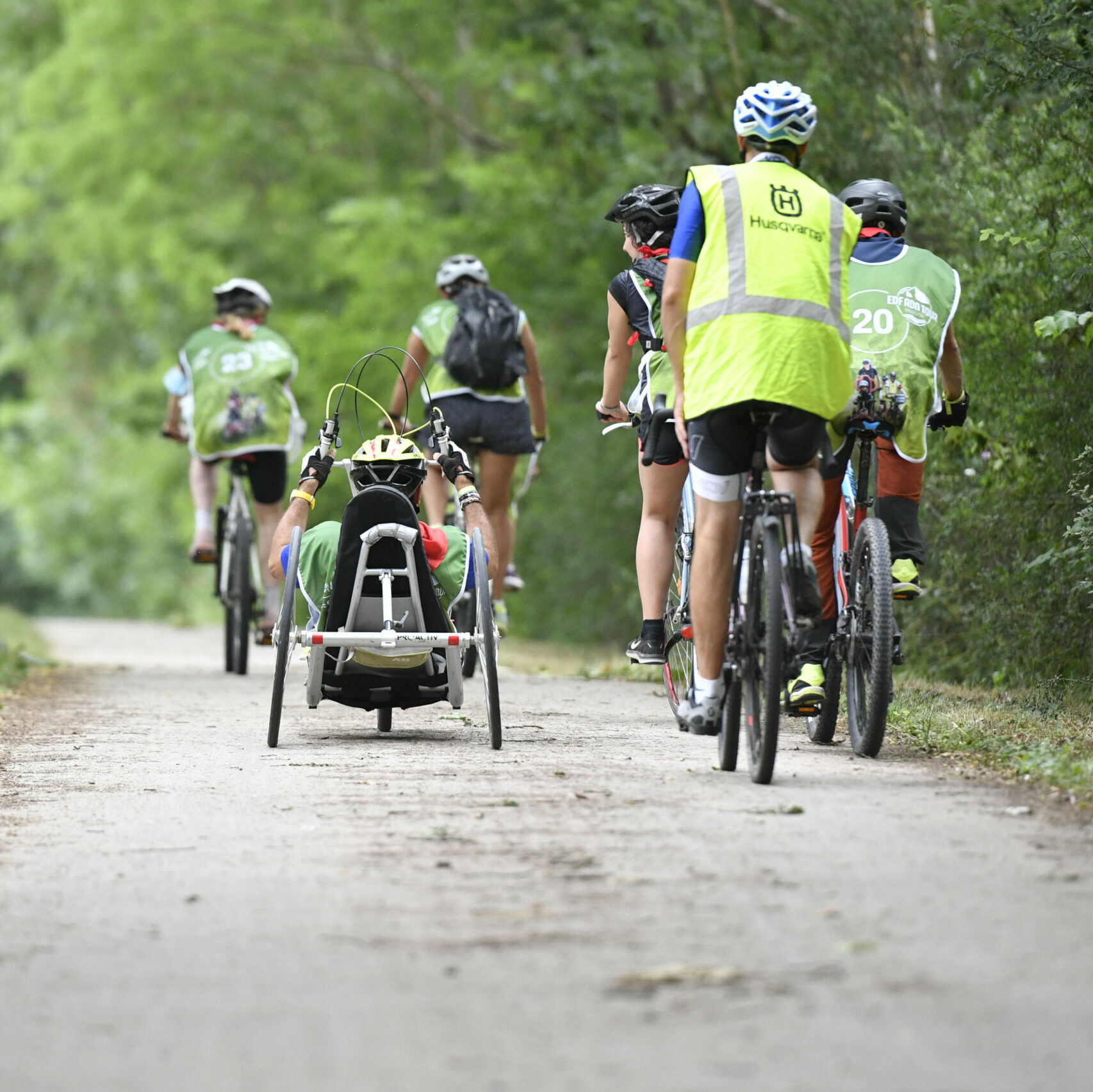 Plusieurs sportifs entrain de faire du cyclisme, certains en solo, d'autres en handbike, pris de dos. 