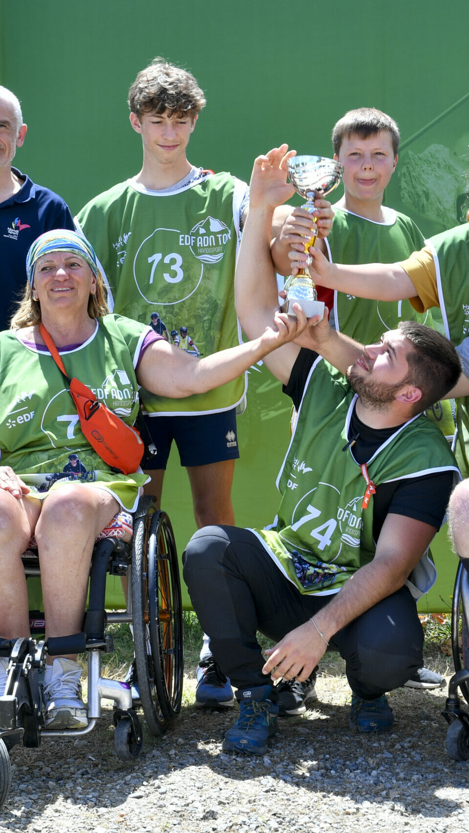Quatre personnes avec des chasubles verts portant une coupe ensemble, pris de face. 
