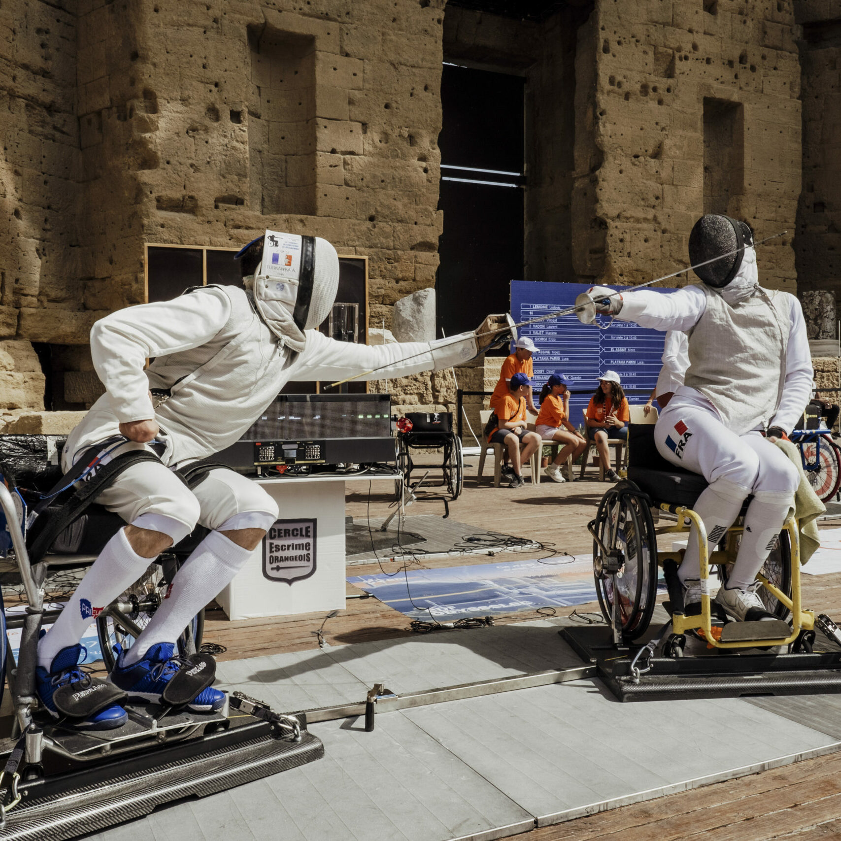 Deux sportifs pratiquant l'escrime dans une arène, l'un des deux tente d'attaquer son adversaire, pris légèrement de côté. 
