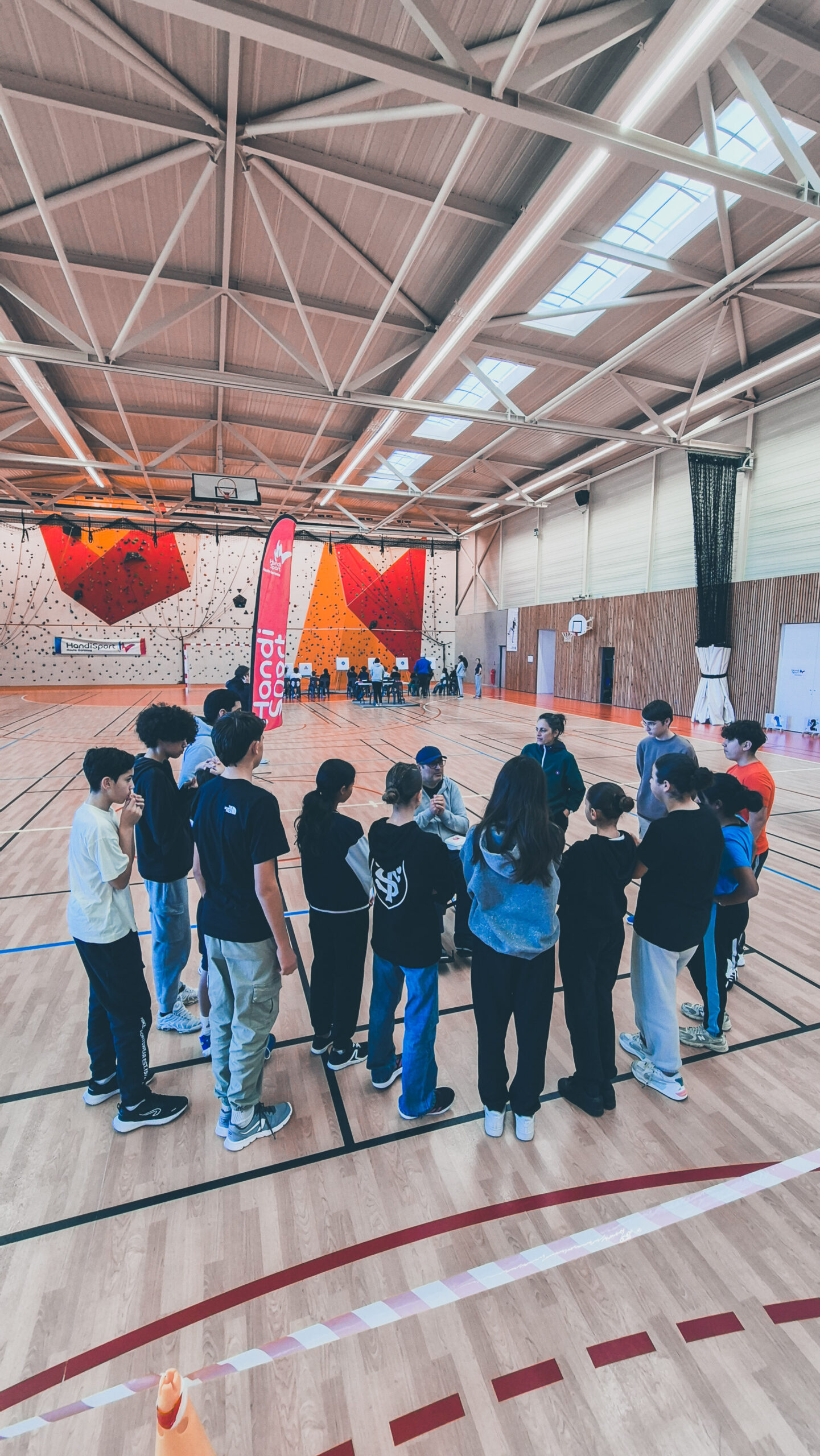 Plusieurs jeunes rassemblés en ronde au fond du gymnase pour tester la sarbacane.