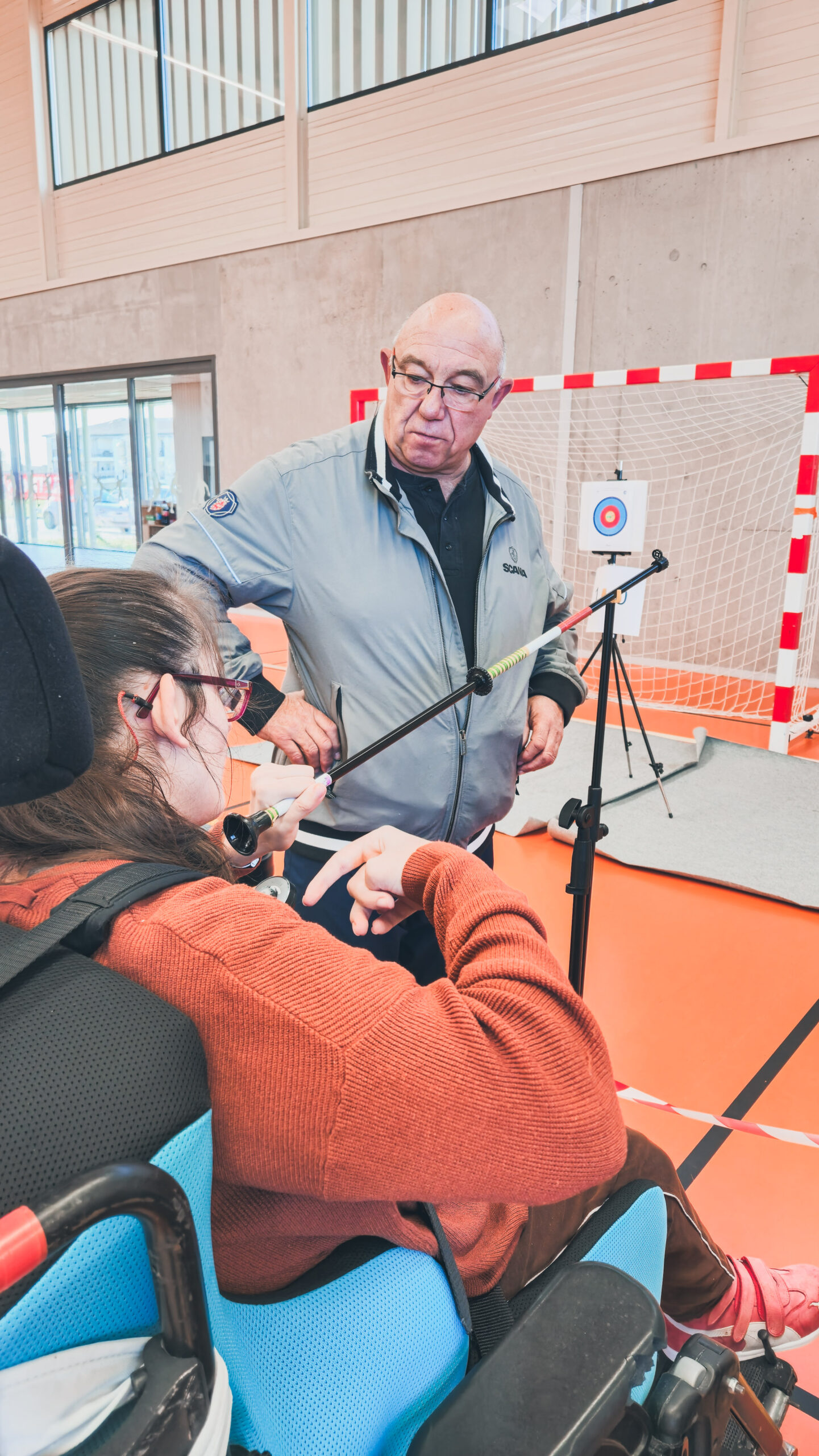 Une sportive avec sa sarbacane maintenue par une potence et son accompagnateur, pris sur le côté.