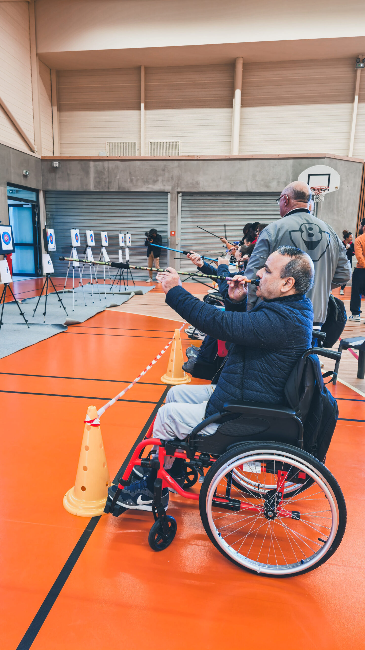 Plusieurs personnes en face des cibles pendant le challenge Sarbacane, un sportif en premier plan tient sa sarbacane et s'apprête à tirer.