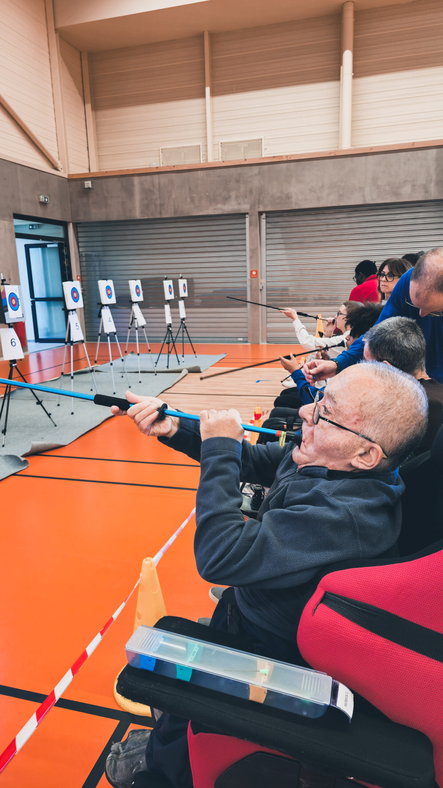 Plusieurs sportifs tirant sur les cibles, trois sarbacanes sont tenues en l'air, pris sur le côté.